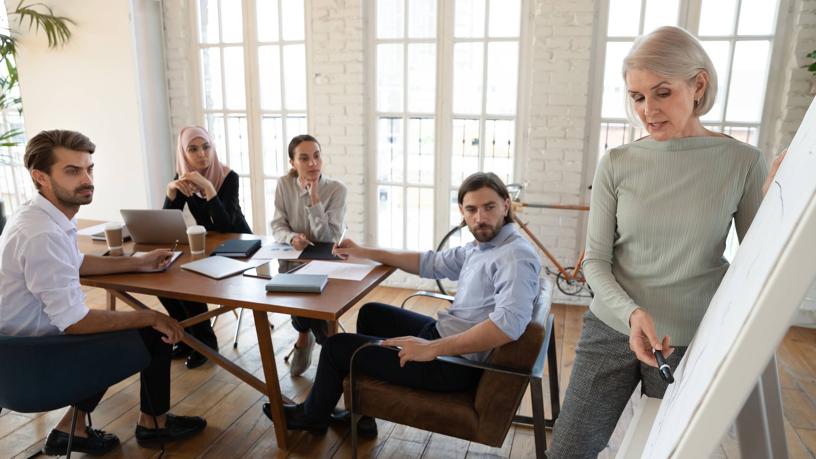Focused multiethnic business people listen old businesswoman coach give presentation